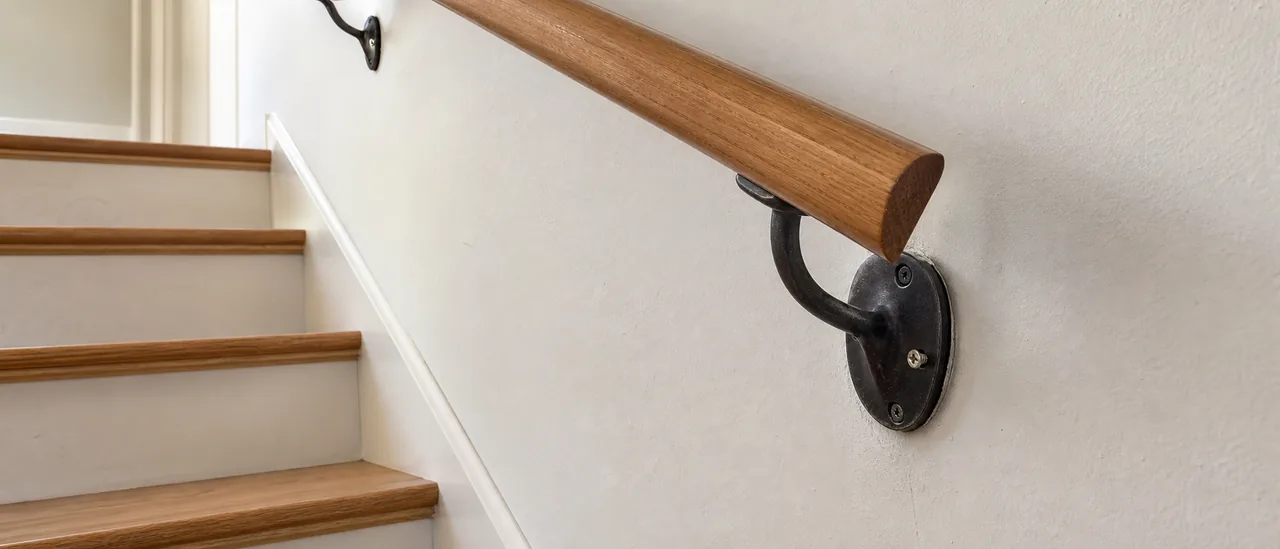Close view of a loose wooden stair handrail pulling away from its wall bracket