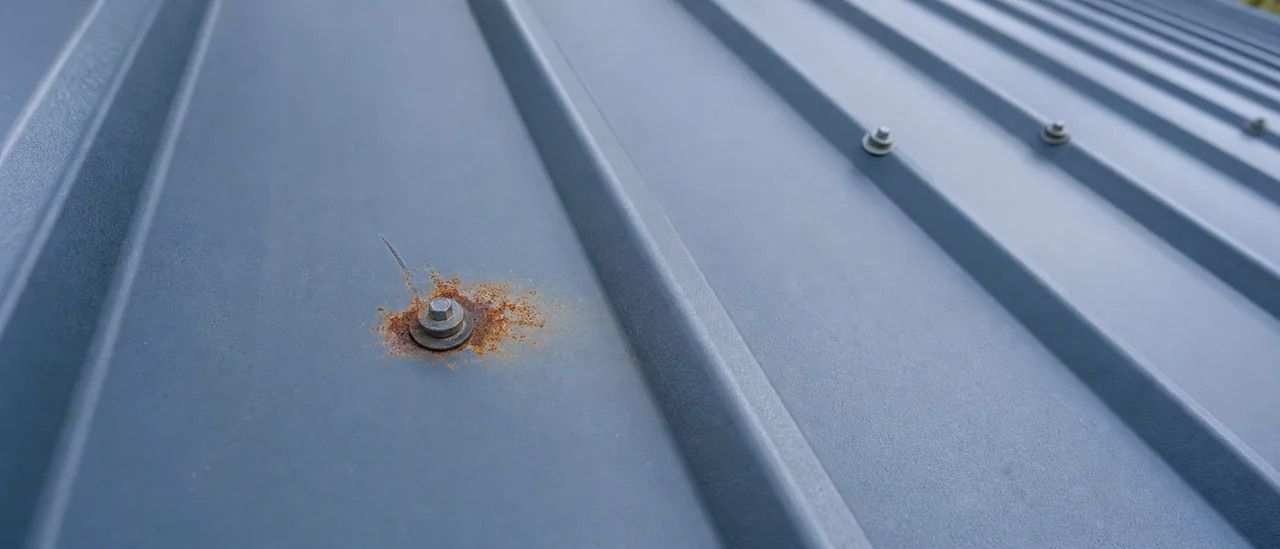 Close view of localized rust around a scratched fastener on a steel roof panel