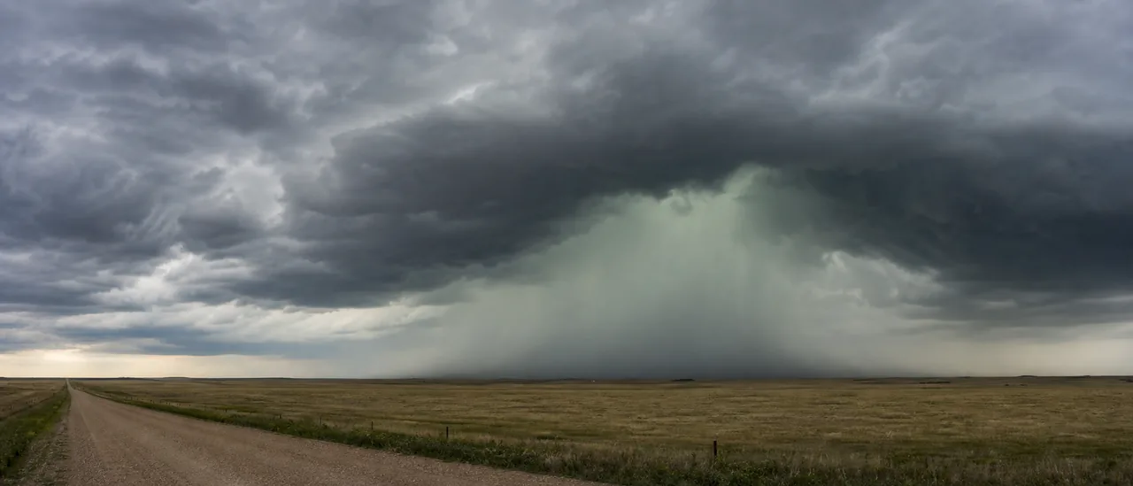 Green-gray light beneath a deep thunderstorm over an open field